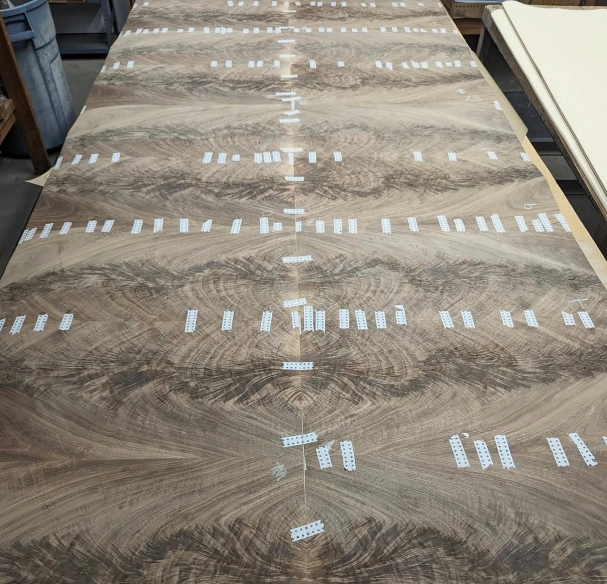 A long run of book-matched crotch veneer taped up on the bench before pressing, the butterfly figure repeating down its length