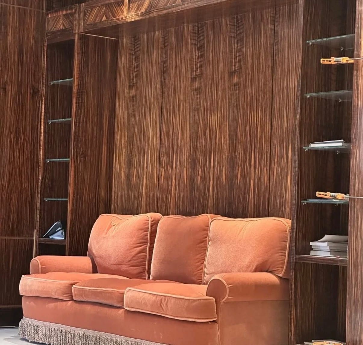A residential interior wall panelled in dark ebony veneer with inset glass display shelving