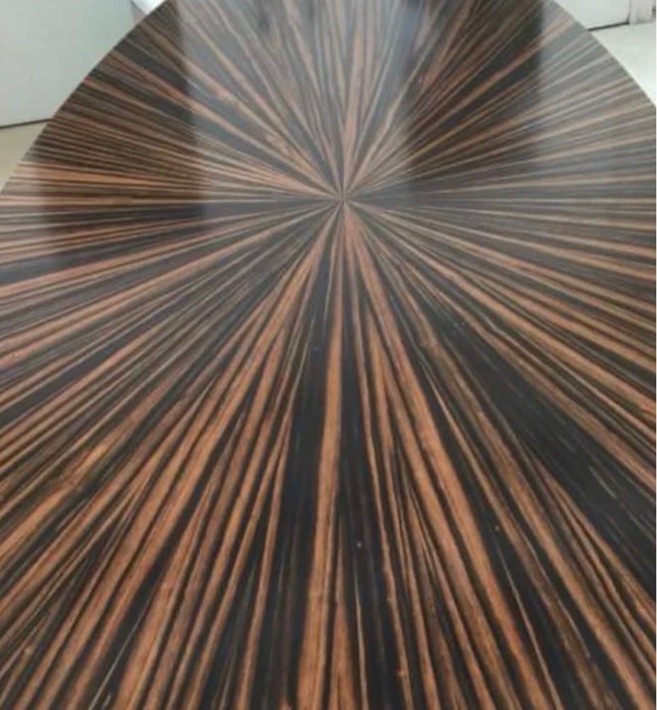 The top of a radial-matched ebony table photographed from above, dozens of tapered leaves radiating from a single point at the centre