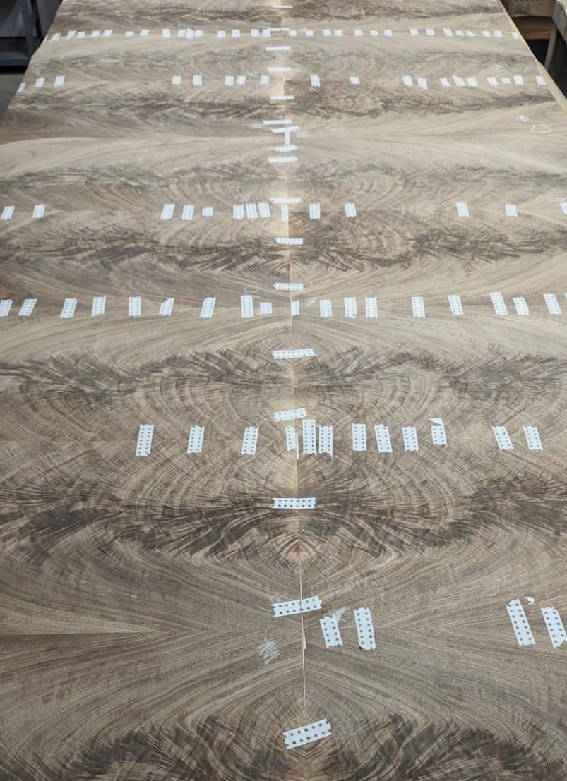 Walnut veneer leaves being laid up and taped on the bench before pressing
