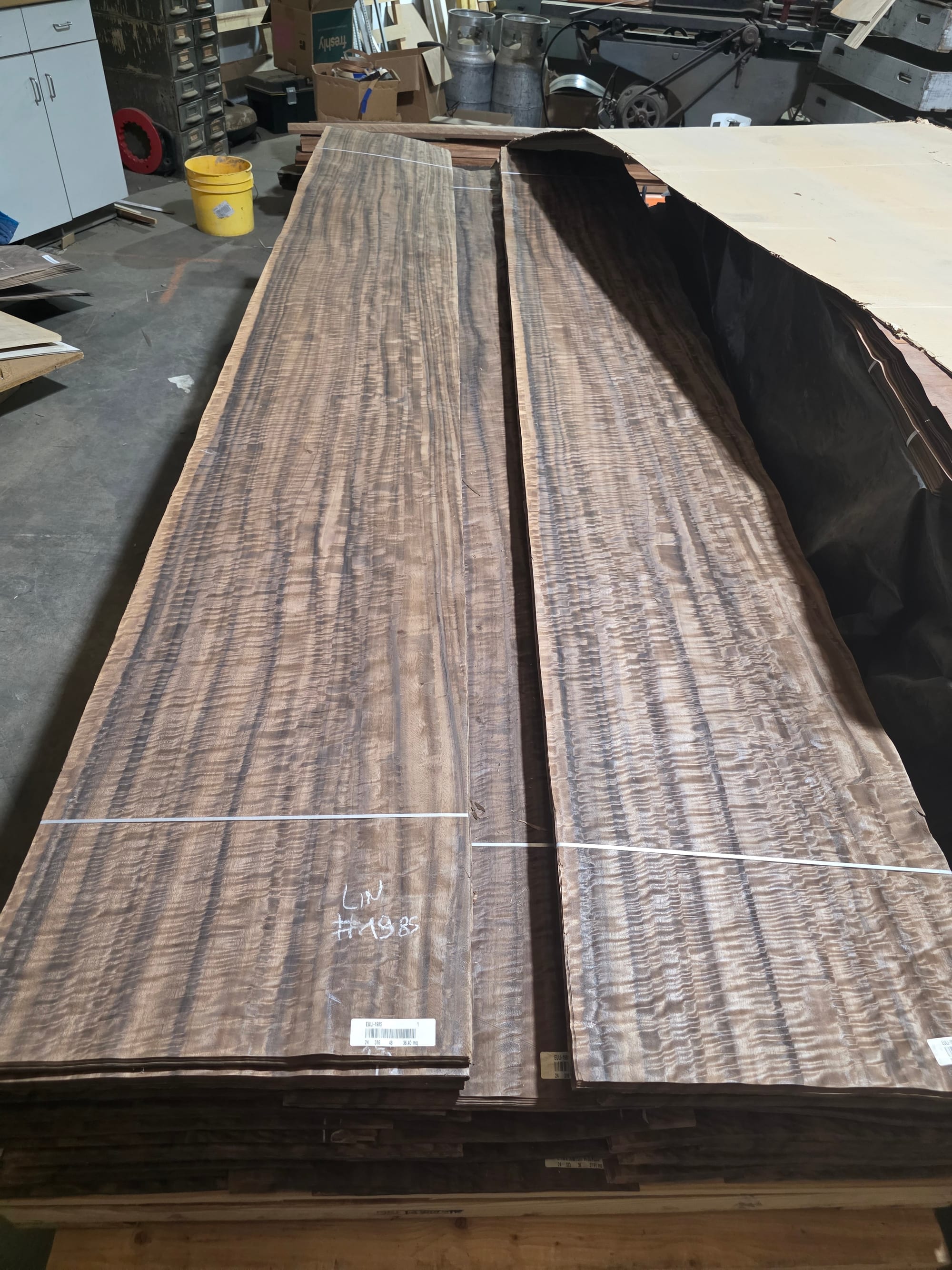 Two long leaves of fumed eucalyptus laid out on a bundled flitch in the shop, each strapped and carrying its grade label